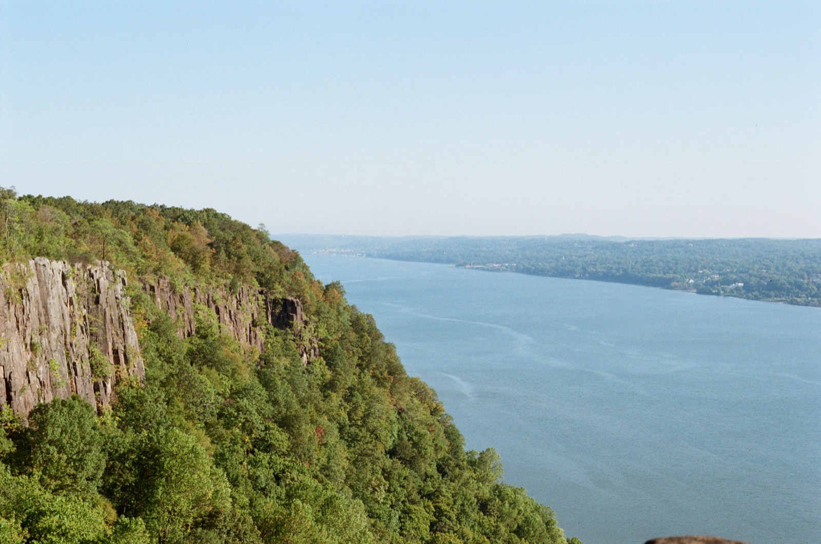 Green, wooded cliffs dropping to a wide river on a clear early-fall day.