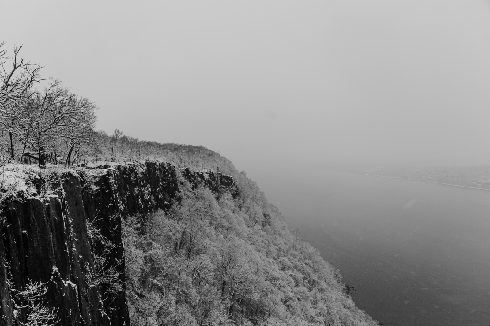 The same cliffs in winter, snow-covered trees on the edge and the river lost in fog, in black and white.