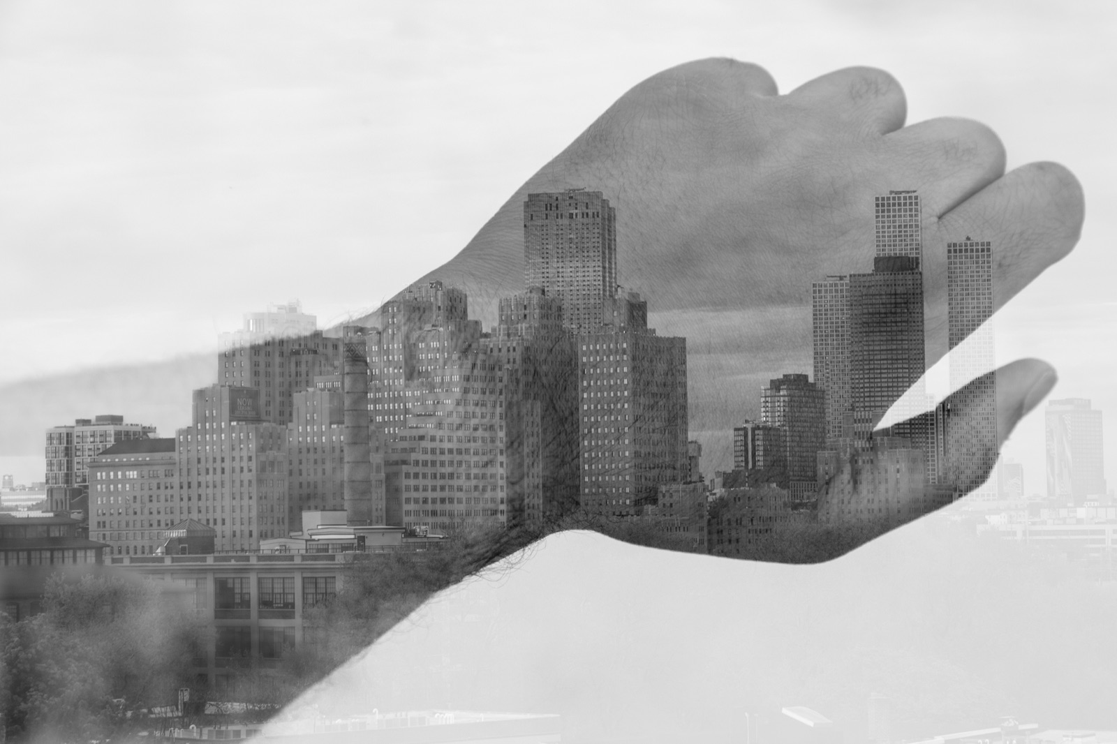 Double exposure of an open hand filled with a city skyline, in black and white.